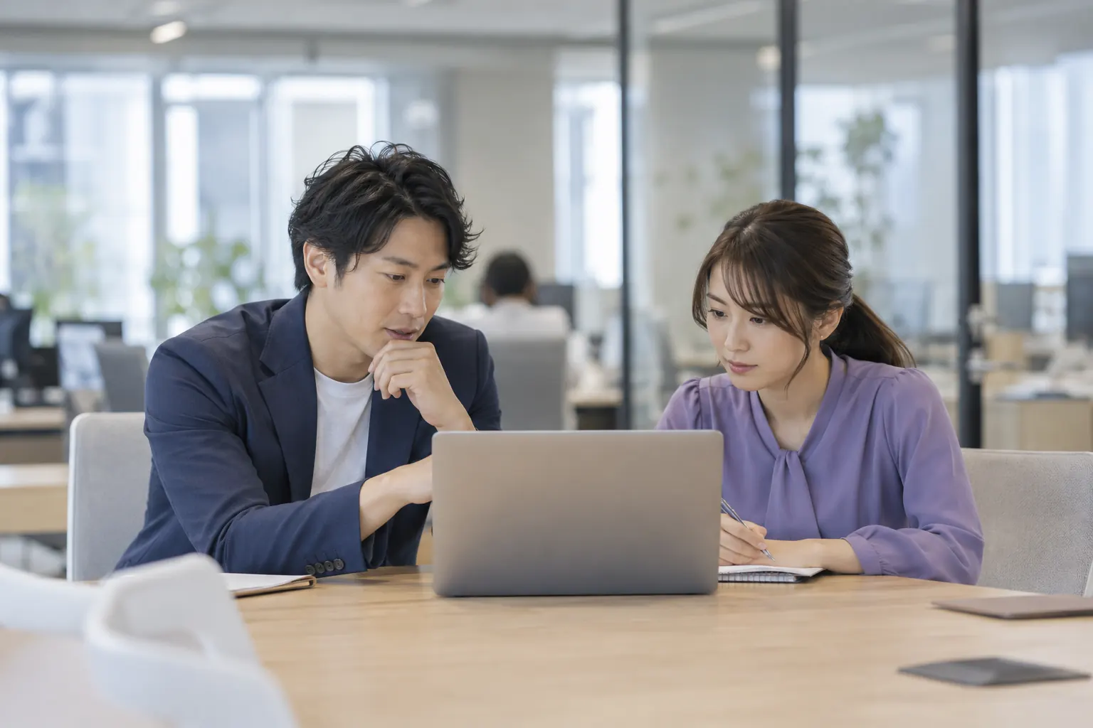 オフィスでノートパソコンを一緒に見ながら話す社員2人